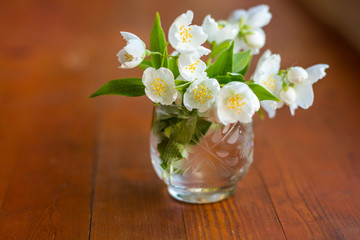 small jasmine bouquet in small glass on a wooden board background