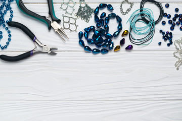 Jewelry findings handmade craft composition with pliers beads embellishments on white wooden...