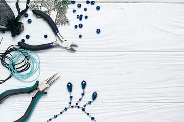 Jewelry findings handmade craft composition with pliers beads embellishments and necklace on white wooden background