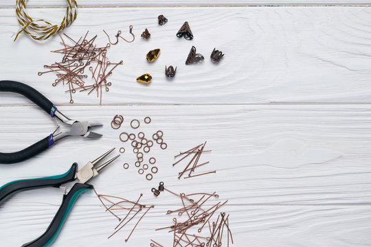 Jewelry findings handmade craft composition with pliers beads embellishments on white wooden background