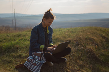 young girl working at laptop with earphones in the fields 