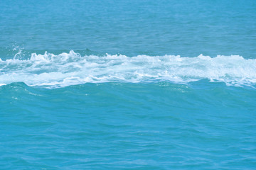 Bubbles of sea waves on the bright blue water surface.