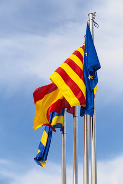 Official flags of the city of Salou, Spain, Catalonia and The European Union EU waving against a blue sky. Vertical.