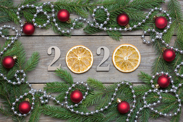 Fototapeta na wymiar 2020 New year rustic background with orange slices, fir tree branches, red baubles and bead chain on wooden boards