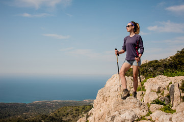 Attractive girl standing on the rock in shorts with walking sticks