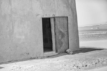 Abstract unreal picture of the corner of a house in the desert with an open blue damaged door of...