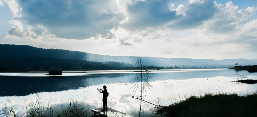 Winter by the lake, traveler woman standing on the terrace and enjoying lake view with camera at sunset, bright clouds and blue sky reflecting on surface of water.
