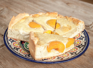 Slices of peach apricot pie or cheese cake on bright oriental plate on wooden table background
