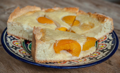 Slices of peach apricot pie or cheese cake on bright oriental plate on wooden table background