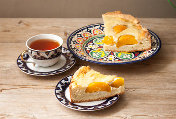 Slice of peach apricot pie or cheese sour cream cake on bright saucer with tea cup on wooden table