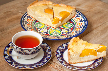 Slice of peach apricot pie or cheese sour cream cake on bright saucer with tea cup on wooden table