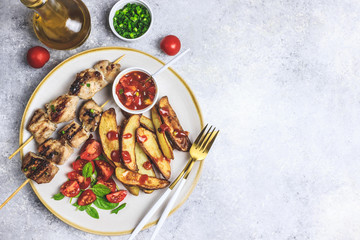Grilled chicken skewers with baked potato, green onion and salsa sauce on a plate on a light gray background. Top view.