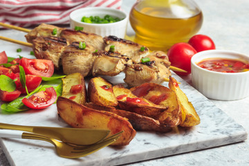 Grilled chicken skewers with baked potato, green onion and salsa sauce on a marble plate on a light gray background. Selective focus