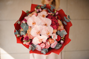 Close up girl in the coat holding a bouquet of pink and red flowers decorated with greenery