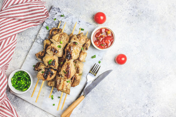 Grilled chicken skewers with green onion and salsa sauce on a marble plate on a light gray background. Top view.