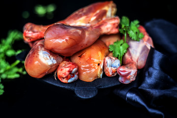 Raw cut unwashed chicken drumsticks in a steel plate isolated in black along with some fresh parsley or coriander leaves on it. Horizontal close up shot.