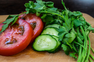 Sliced ​​tomatoes and parsley with cucumbers for salad, vegetarian food on a cutting board close-up