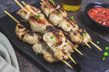 Grilled chicken skewers with green onion and salsa sauce in a cutting board on a dark background. Selective focus