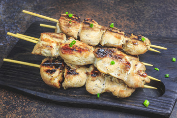 Grilled chicken skewers with green onion and salsa sauce in a cutting board on a dark background. Selective focus