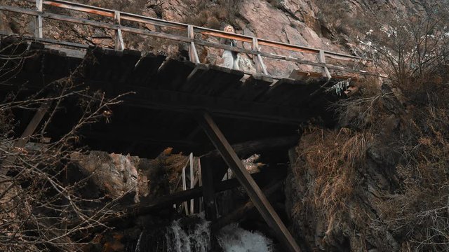 Tourist with a camera is an old wooden bridge in the rocks, taking pictures. Free travel, girl photographer looking for a place to shoot, walk, shoot. Bottom view, slow motion, 4K