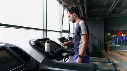 Fototapeta na wymiar Young man in sportswear running on treadmill at gym. Healthy lifestyle and sports concept