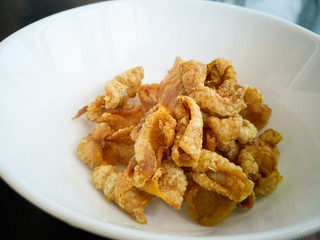 Close up of deep-fried chicken skins in a white bowl.