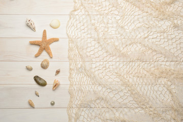 Fototapeta na wymiar Conchas, estrella de mar y caracolas marinos sobre fondo de madera blanca con red de pescar