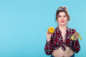 Pin-up woman with measuring tape and doughnut over blue background with copy space