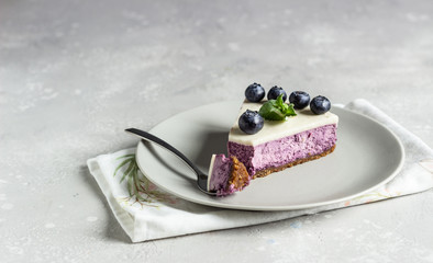 Piece of blueberry cheesecake, fresh blueberries and mint on a light stone background. Copy space.