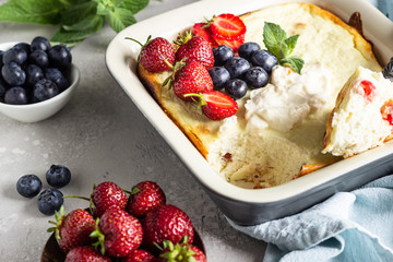 Cottage cheese (twarog or farmers cheese) baked pudding, strawberries, blueberries, sour cream and mint on a light stone background. Summer breakfast. Healthy food.