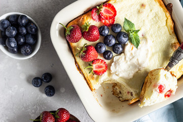 Cottage cheese (twarog or farmers cheese) baked pudding, strawberries, blueberries, sour cream and mint on a light stone background. Summer breakfast. Healthy food.