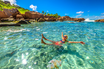 Swimming pool at Anse Cocos in La Digue. Happy woman in bikini lying on turquoise water of natural pool at Anse Cocos Beach protected by rock formations. Joyful girl at crystal lagoon at Seychelles.