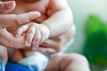 An Asian baby boy does not wear clothes to catch his mother's fingers.