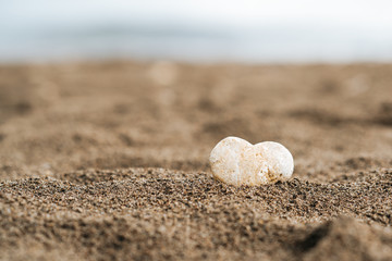 Gray stone in the form of heart lies on sand.