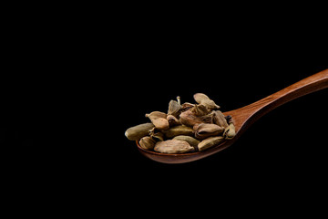 Cardamom seeds on wooden spoon over black background. 
