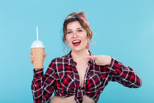 Beautiful positive young girl in a red checkered shirt and headbands holds a cocktail in her hands and shows with a finger posing for a blue background. Concept of desserts and cocktails.