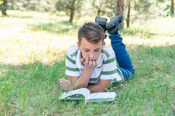 The boy lies in the park on the grass and is studying in nature, education and science, the book is lying on the grass.