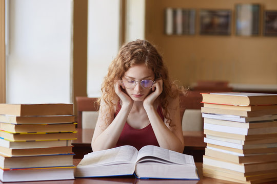 Image of woman teenager sitting in reding room, lady reading book, preparing for final examination, finding out information, has concentrated facial expression. Students and knowladge concept.