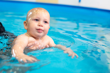 Fototapeta na wymiar Cute sad baby boy learning to swim in special pool for little children