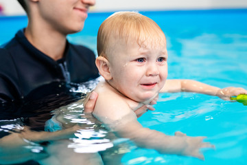 Cute sad baby boy learning to swim in special pool for little children
