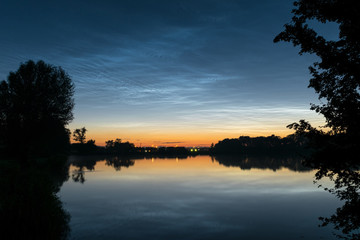 NLC: noctilucent clouds over northwestern Europe, seen from the shore of a lake at night on a calm night