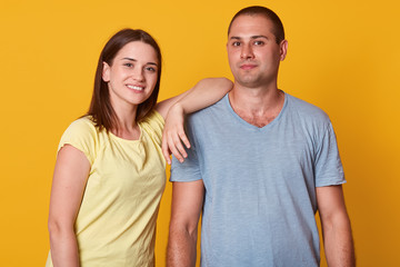 Closeup portrait of happy peaceful couple, standing isolated over yellow background in studio, smiling sincerely, being close to each other, looking directly at camera, wearing casual clothes.