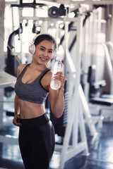 Sporty Asian Woman hold bottle of water with Exercise Equipment Background. Smiling attractive...