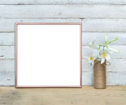 Rose Gold square Frame mockup near a bouquet of lilies stands on a wooden table on a painted white wooden background. Rustic style, simple beauty. 3 render.