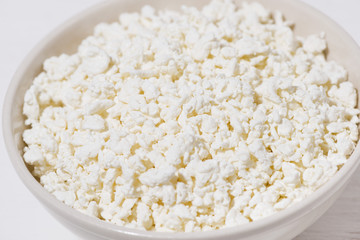 bowl of fresh farm cottage cheese on a white wooden background, closeup