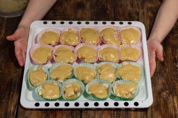 A cook holds muffins on a baking sheet. Baking tray filled with cupcakes.