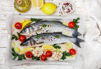 Two raw fresh sea bass ready for baking with tomatoes, lemon, red onion, garlic, ginger, parsley and spices. Prepare a tasty and healthy lunch or dinner in a Mediterranean style. Selective focus