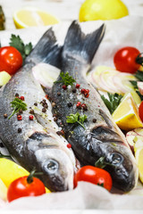 Two raw fresh sea bass ready for baking with tomatoes, lemon, red onion, garlic, ginger, parsley and spices. Prepare a tasty and healthy lunch or dinner in a Mediterranean style. Selective focus