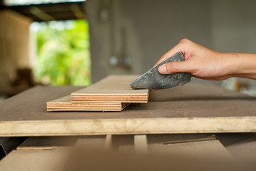 Selective focus on a hand of carpenter holds the sand paper and scrubs on the wood surface at the factory