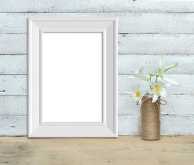 Vertical A4 Vintage White Wooden Frame mockup near a bouquet of lilies stands on a wooden table on a painted white wooden background. Rustic style, simple beauty. 3d render.
